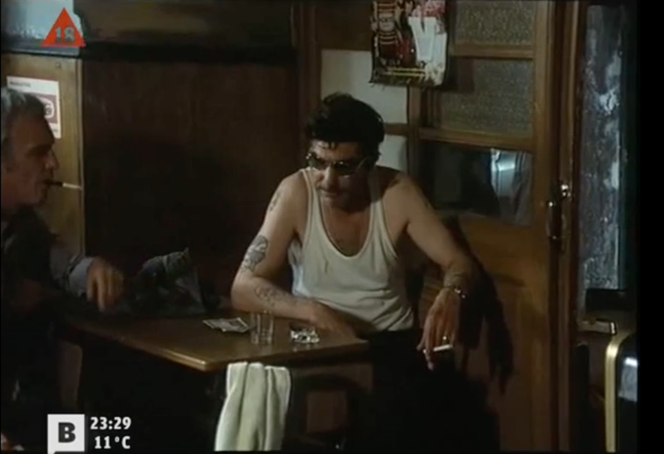 Photogramme tiré du film Tatuaje.
On voit deux hommes accoudés à une table en train de fumer.